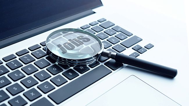 There is a magnifying glass on the laptop keyboard. In the magnifying glass you can see the word "Jobs".